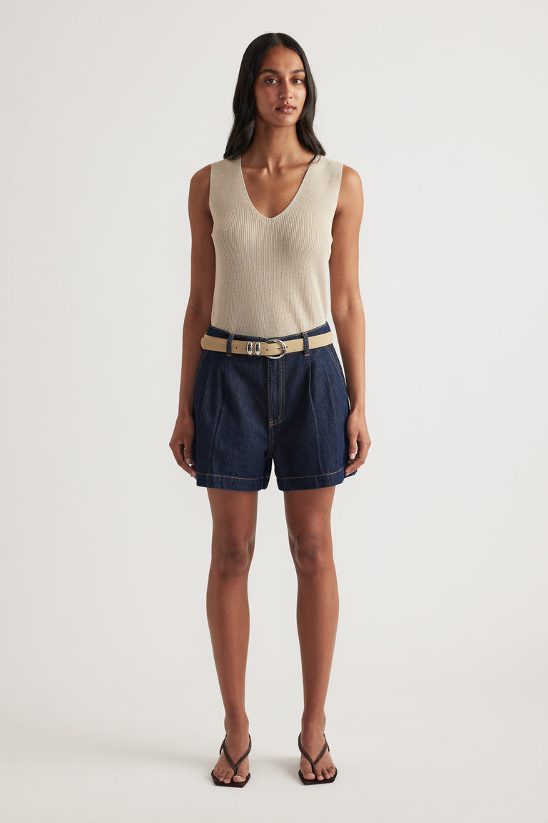 Model wearing high rise navy denim shorts with pleat detailing, a belt and cream knit tank top
