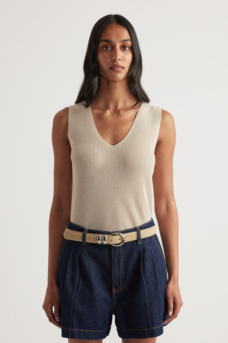 Woman wearing a beige metallic knit tank with a low V neckline and dark denim shorts
