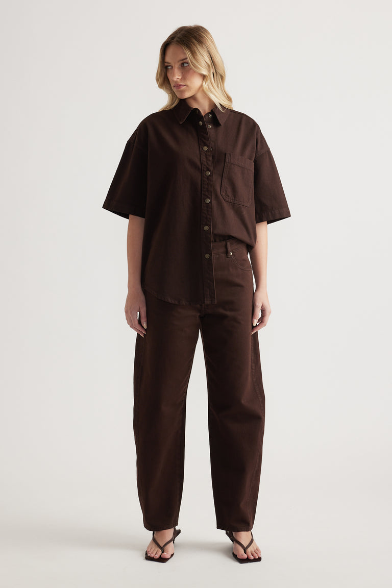 Woman wearing an oversized brown denim shirt with matching barrel leg jeans and strappy flat sandals