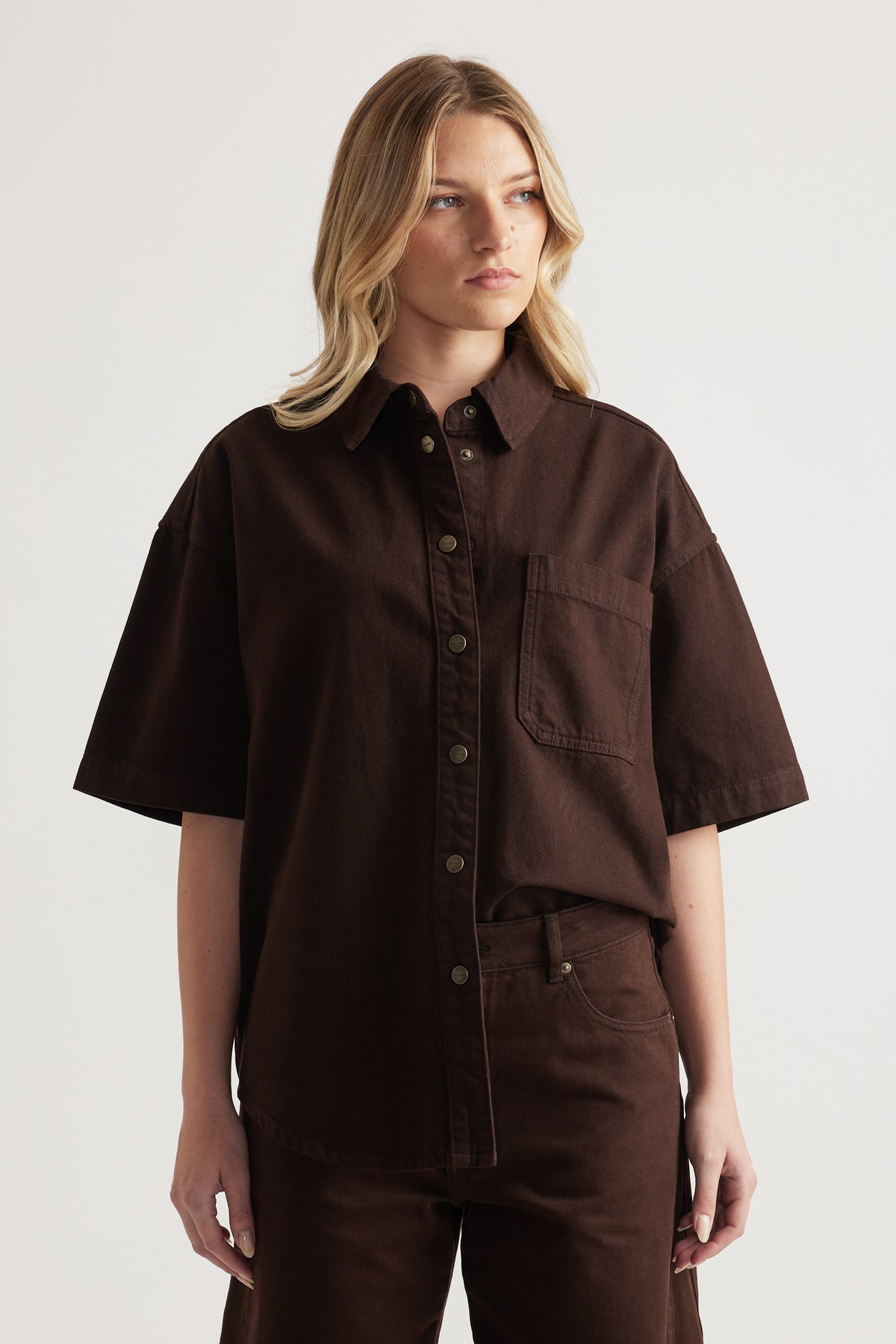 Woman wearing an oversized brown denim shirt with short sleeves and matching jeans