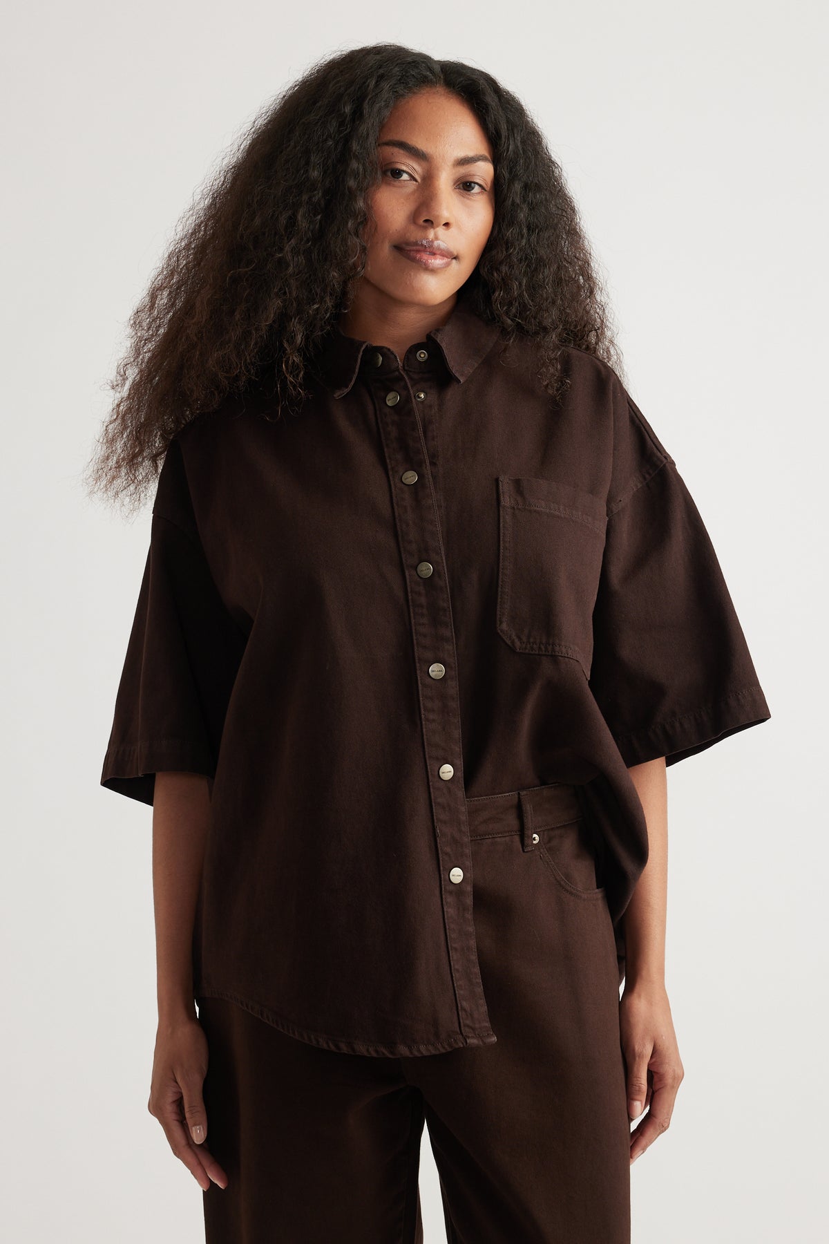 Woman wearing an oversized dark brown denim shirt with short sleeves and matching pants
