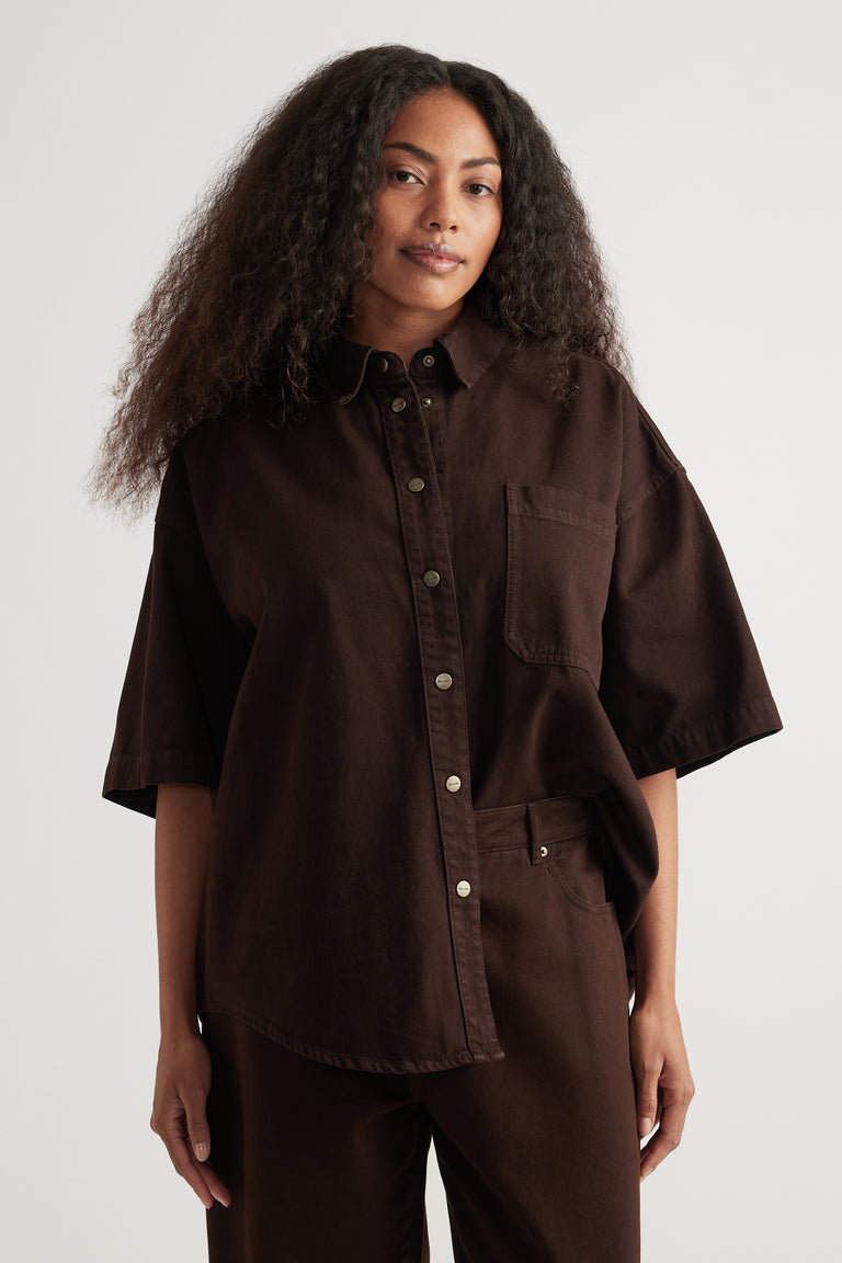 Woman wearing an oversized dark brown denim shirt with short sleeves and matching pants
