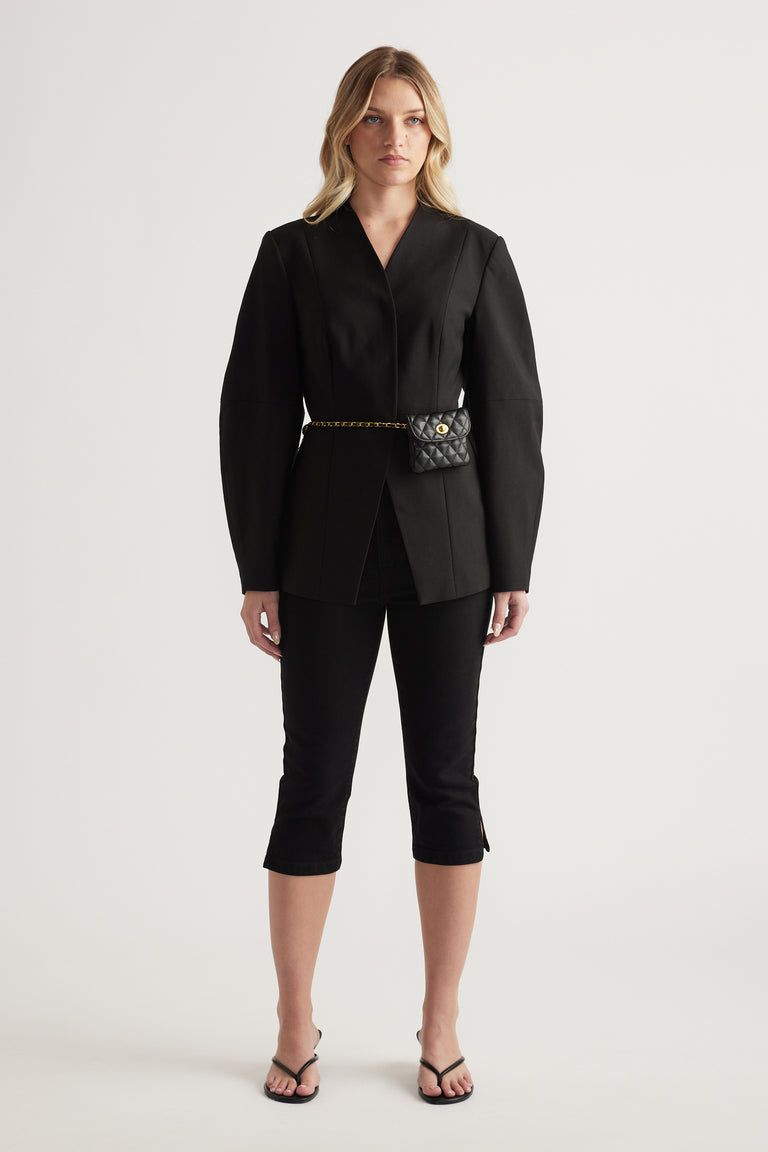 Woman wearing a black blazer with black denim capri pants and strappy sandals