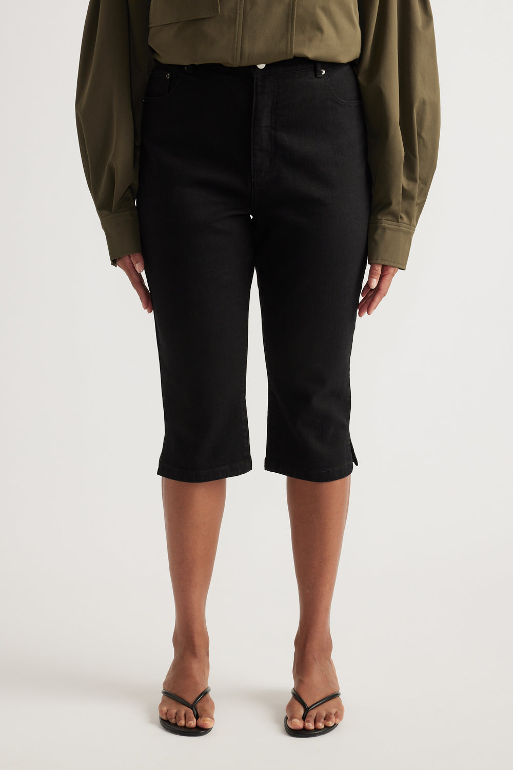 Woman wearing black high-rise denim capris with an olive shirt and strappy sandals