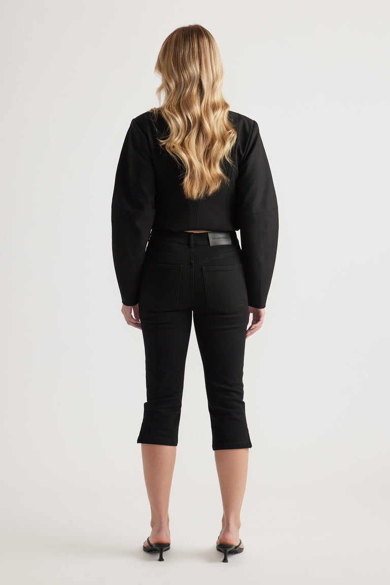 Woman viewed from behind wearing a black top with black denim capri pants and heels