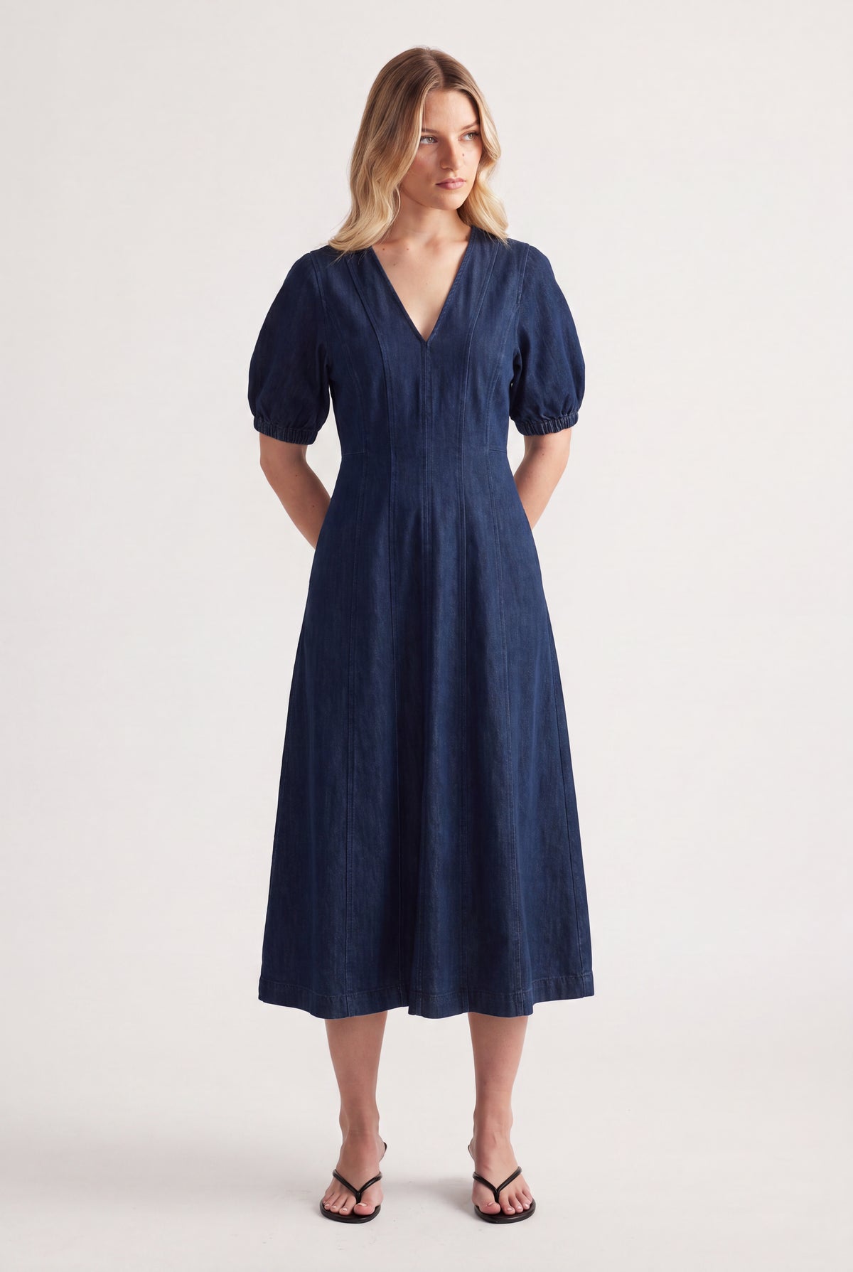 Woman wearing a dark blue panelled denim midi dress with puff sleeves and black sandals