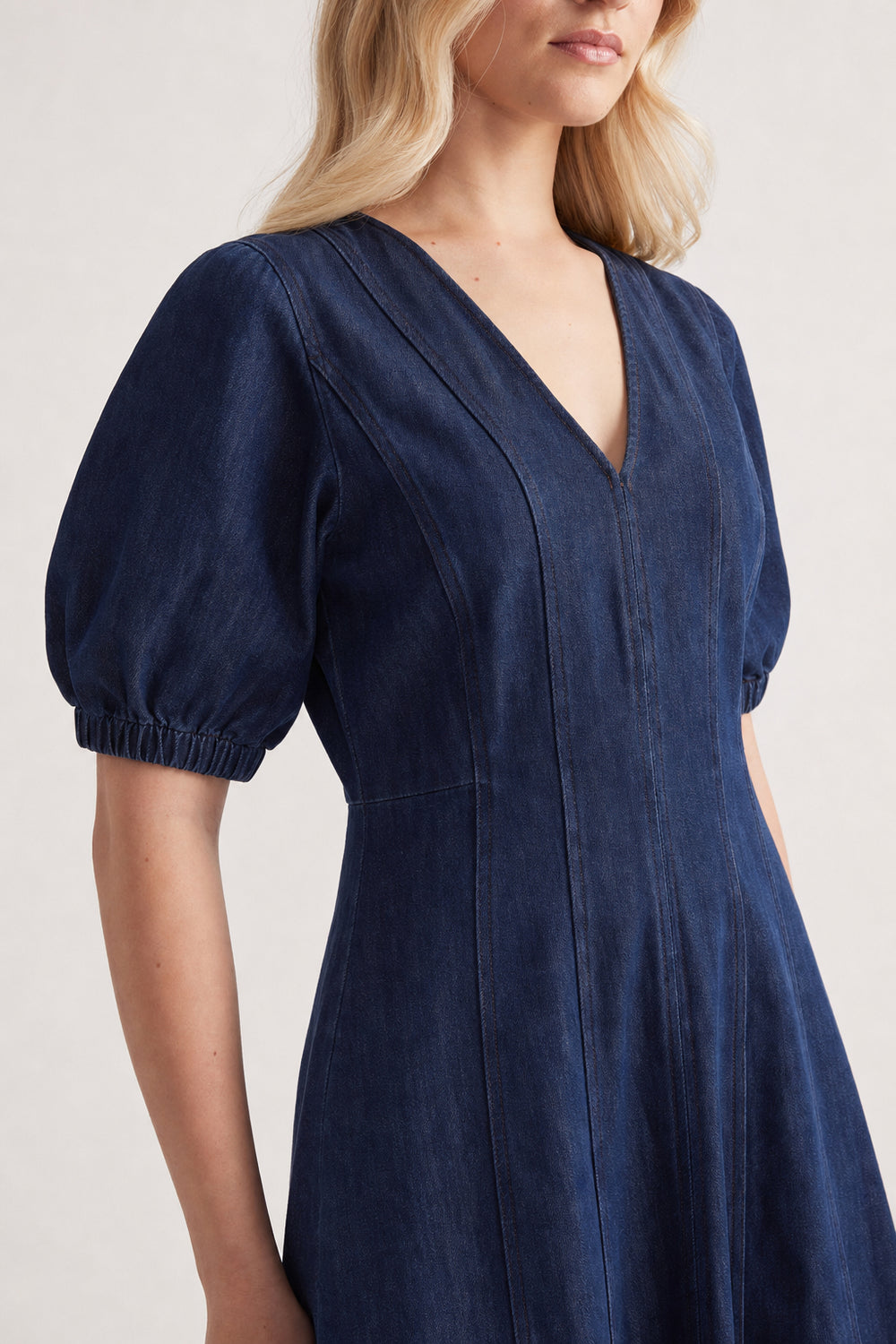 Woman wearing a dark blue panelled denim midi dress with puff sleeves and a V-neckline