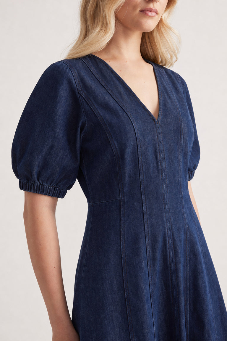 Woman wearing a dark blue panelled denim midi dress with puff sleeves and a V-neckline