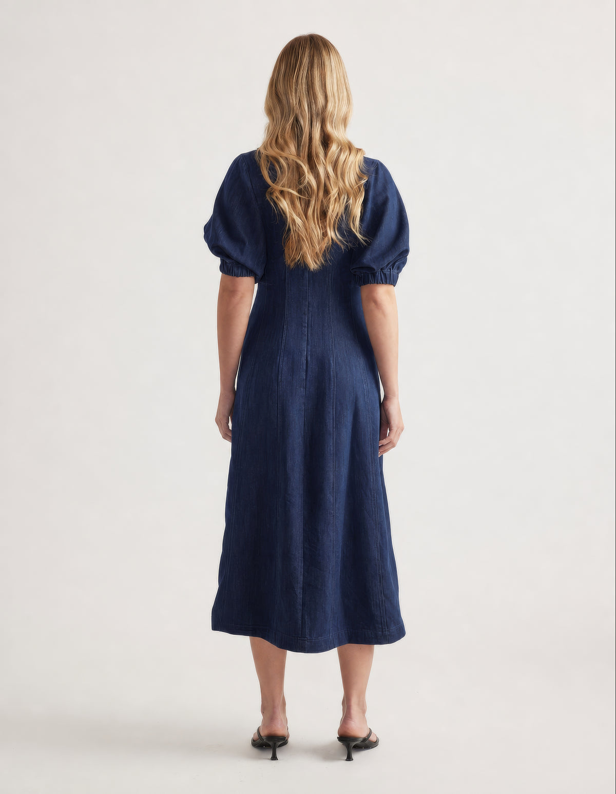 Back view of a woman wearing a navy denim midi dress with puff sleeves and an A line silhouette