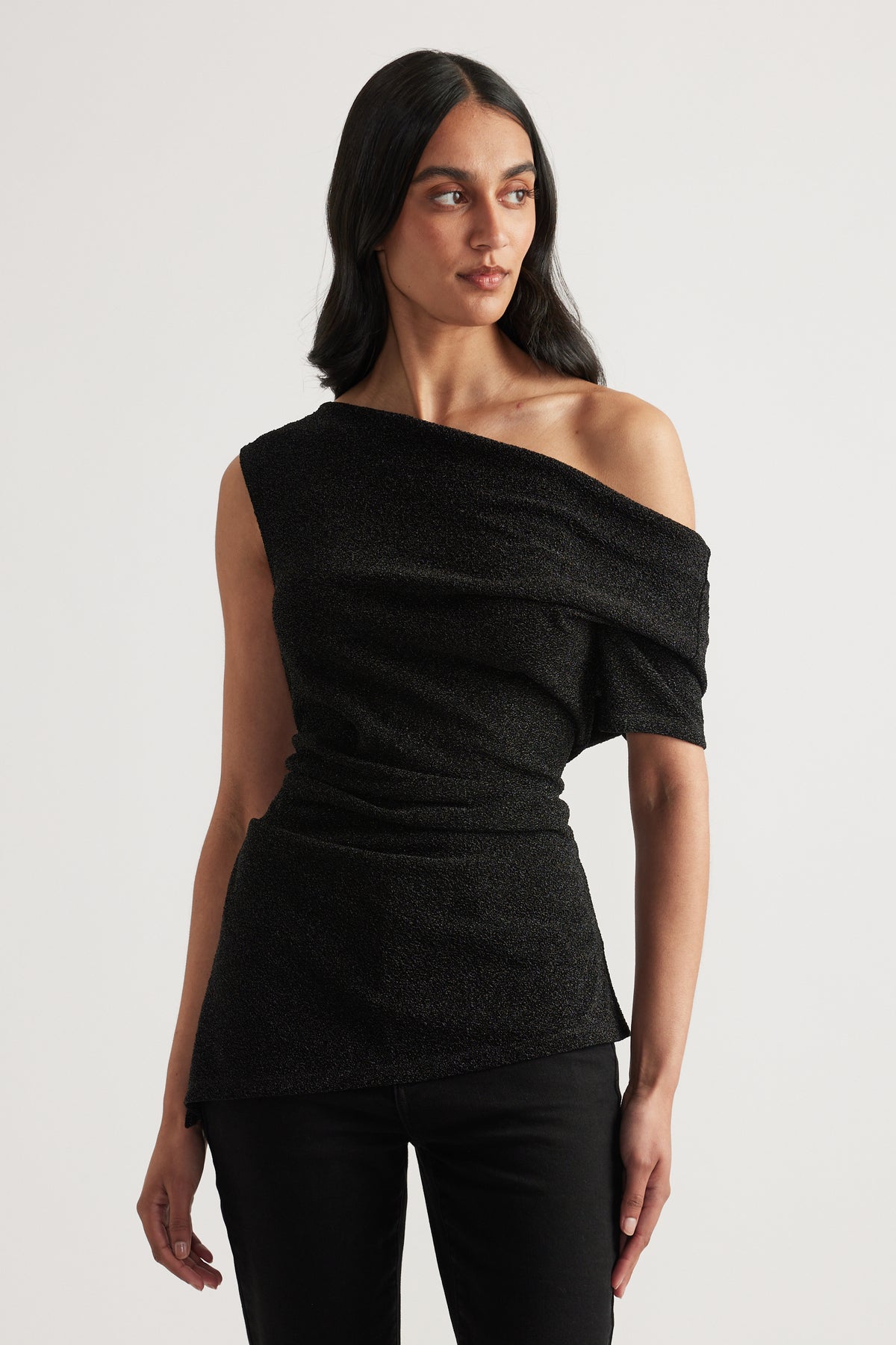 Woman wearing a black off shoulder top with an asymmetric neckline and hem