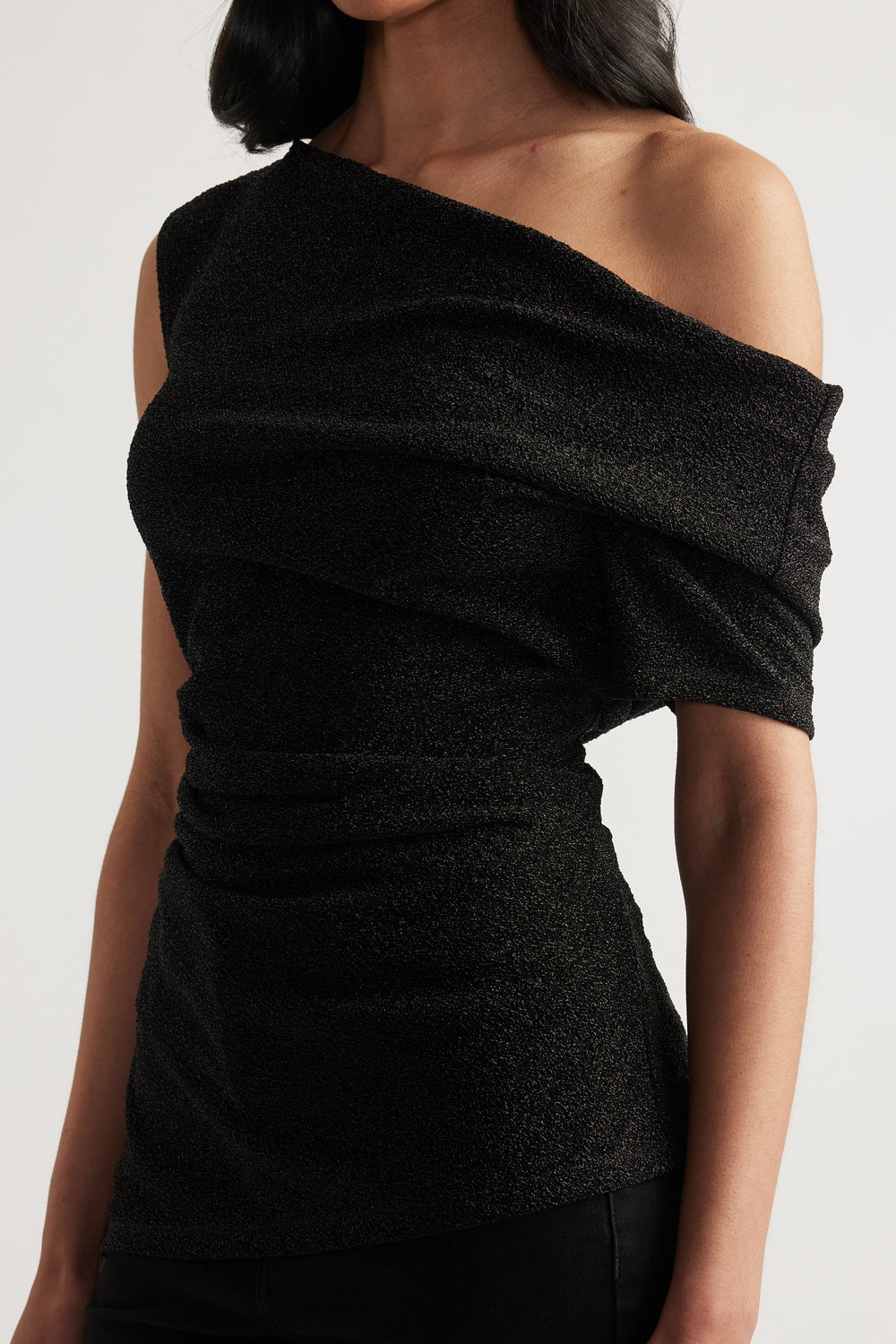 Woman wearing a black off shoulder top with an asymmetric neckline and ruched waist detail