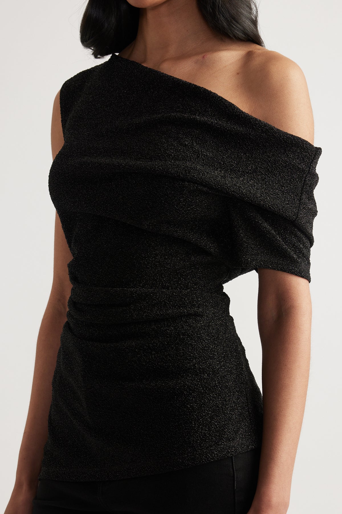 Woman wearing a black off shoulder top with an asymmetric neckline and ruched waist detail