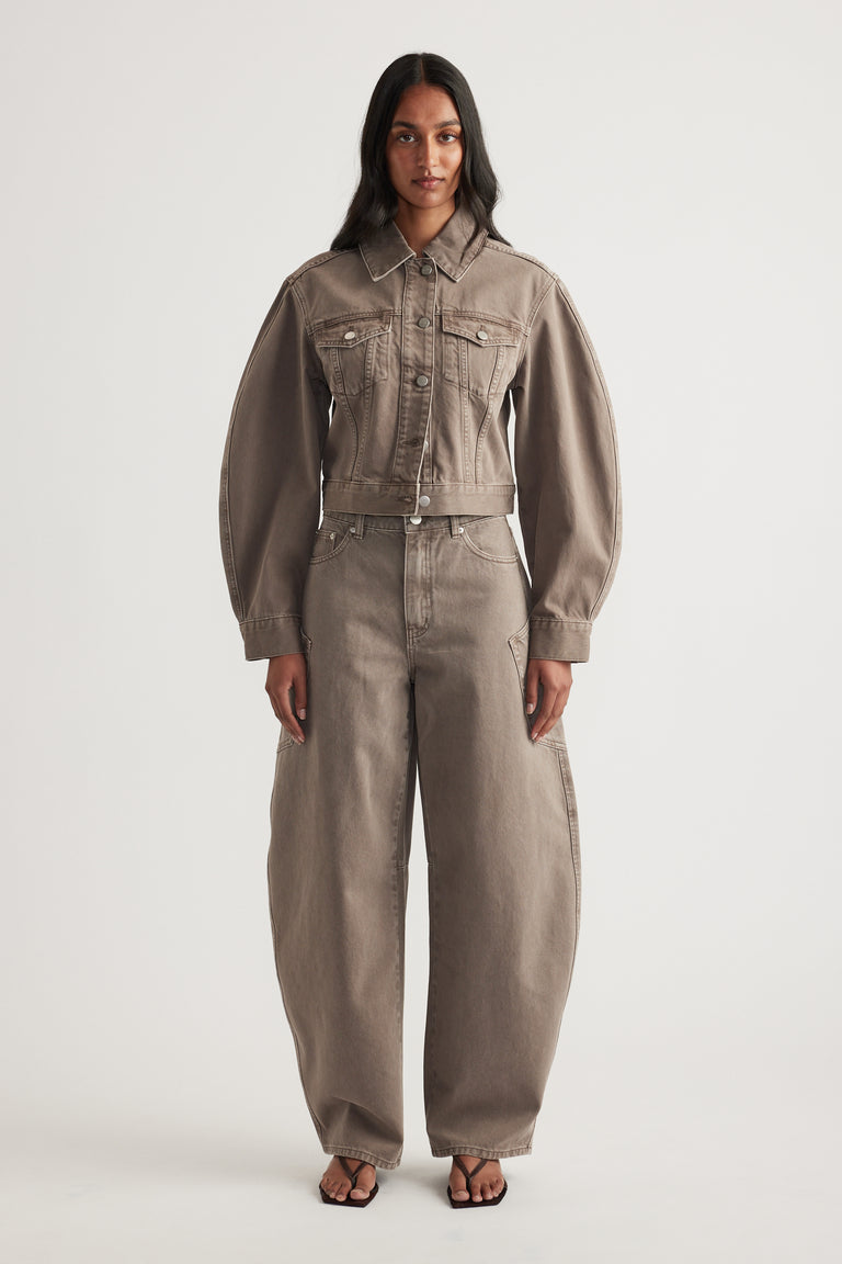 Model in a cropped taupe denim jacket with chest pockets, matching barrel leg jeans and black sandals