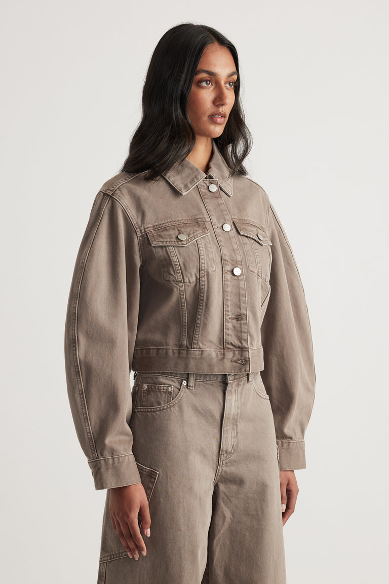 Woman wearing a taupe cropped denim jacket with chest pockets and matching high waist jeans