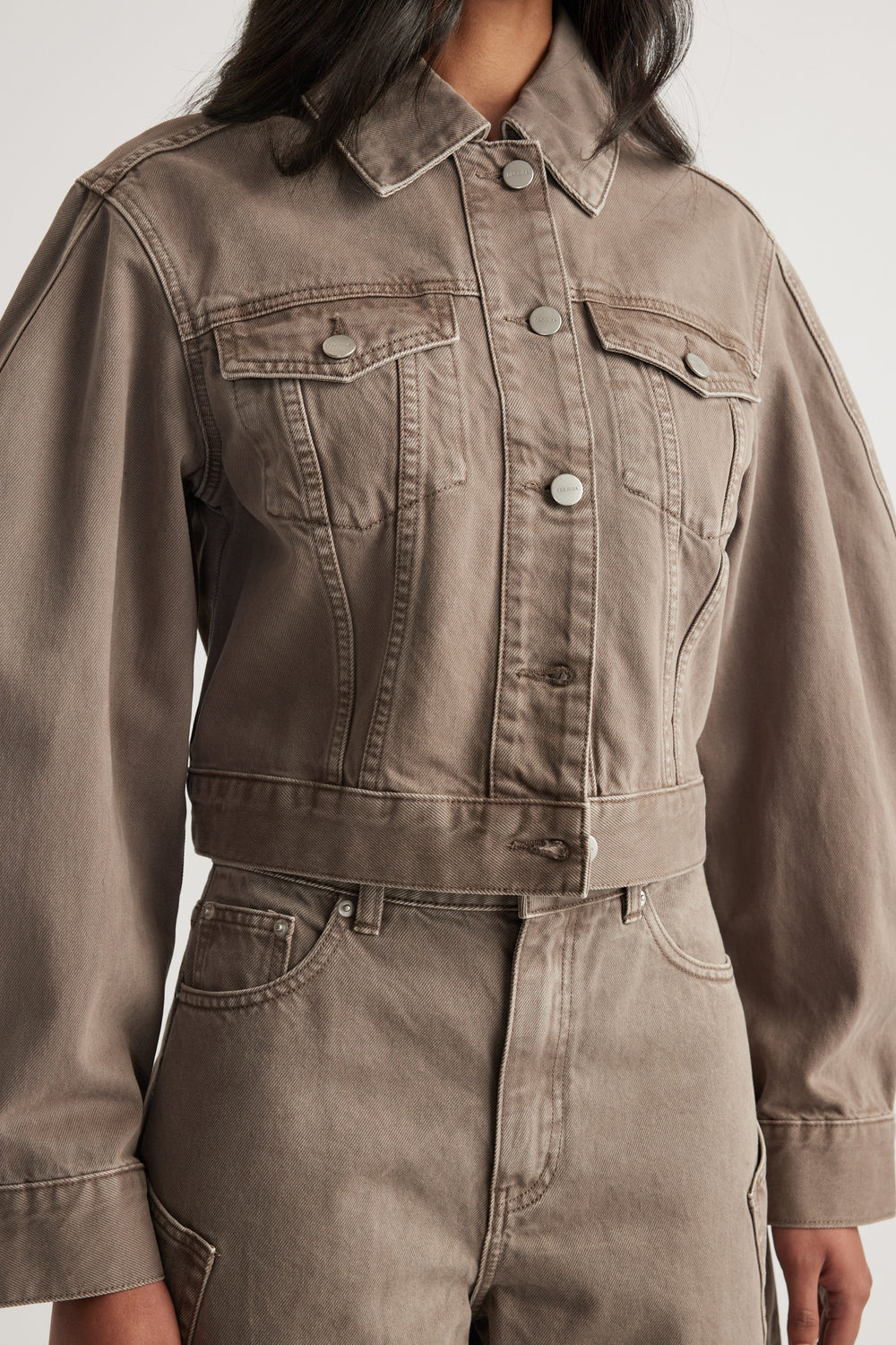 Woman wearing a taupe cropped denim jacket with long sleeves, chest pockets and matching jeans