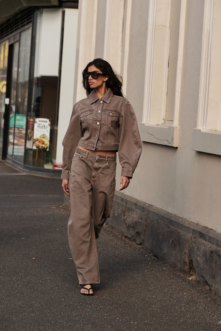 Woman wearing a brown denim jacket with matching high rise barrel leg jeans and sunglasses