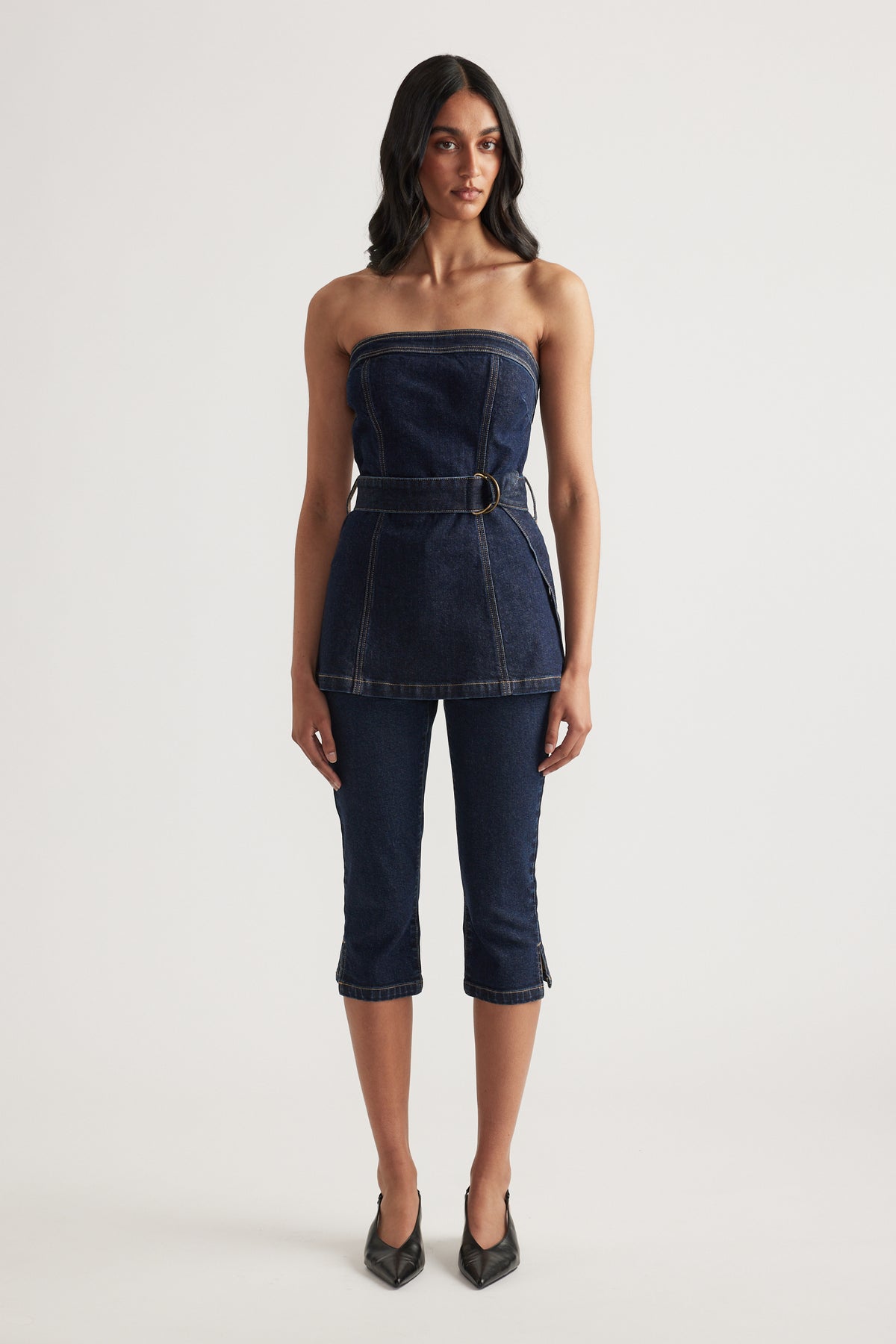Woman wearing a dark denim strapless top with a belted waist, cropped denim jeans and black heels