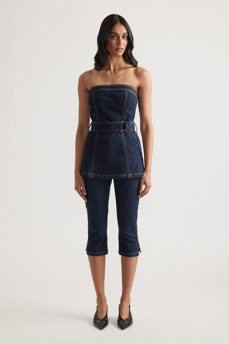 Woman wearing a dark denim strapless top with a belted waist, cropped denim jeans and black heels