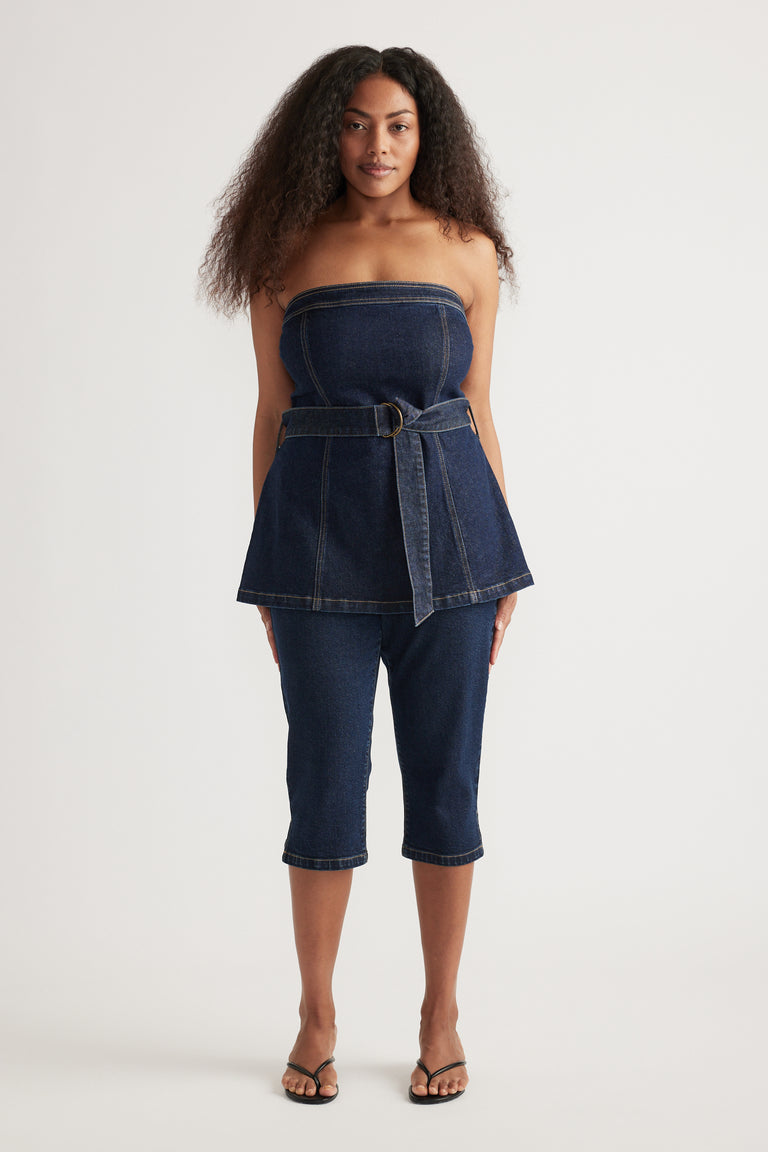 Model wearing a strapless dark denim top with a waist belt, matching capri jeans and flat sandals