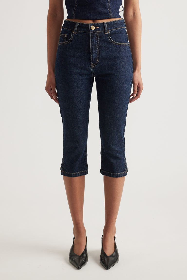Woman wearing high rise dark wash denim capri pants with a slim fit and black pointed heels