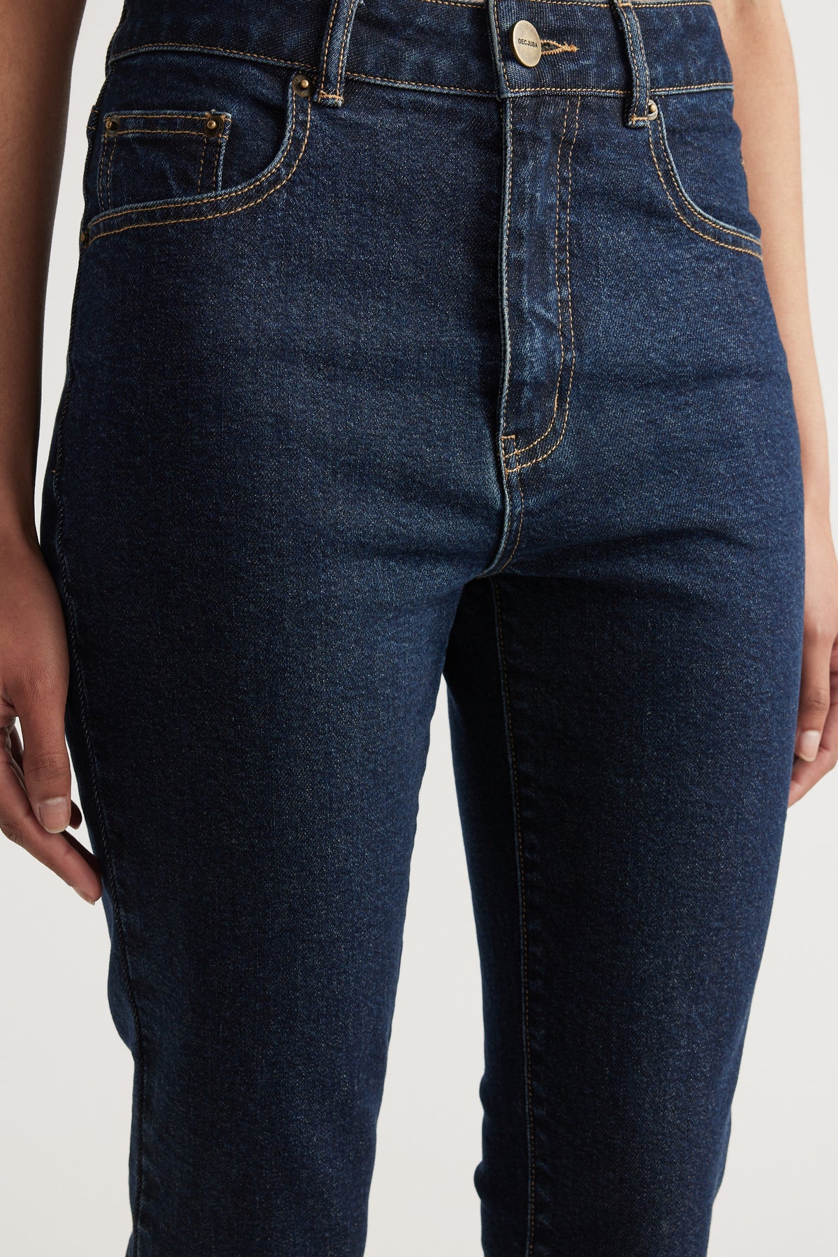 Model wearing dark indigo high rise slim leg denim capris with contrast stitching