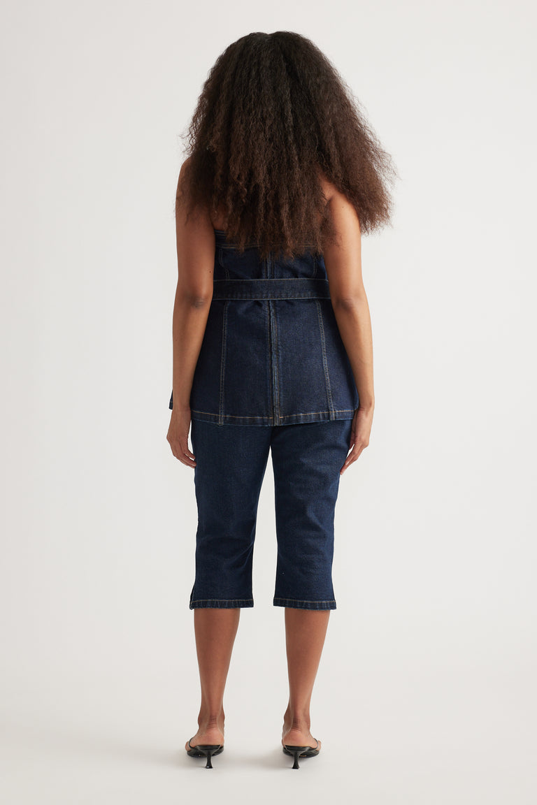 Back view of a model in a dark denim strapless longline top with matching capri jeans and heels