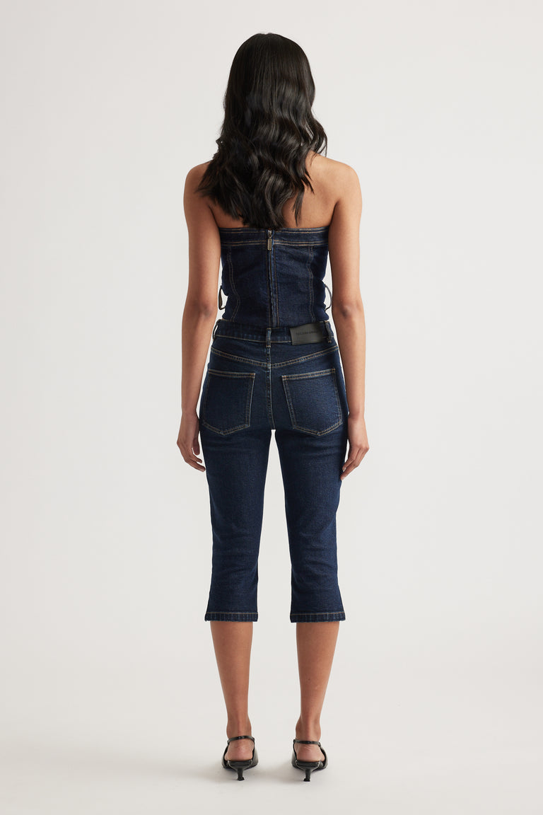 Back view of a woman wearing a strapless denim top with matching dark denim capri jeans and heels