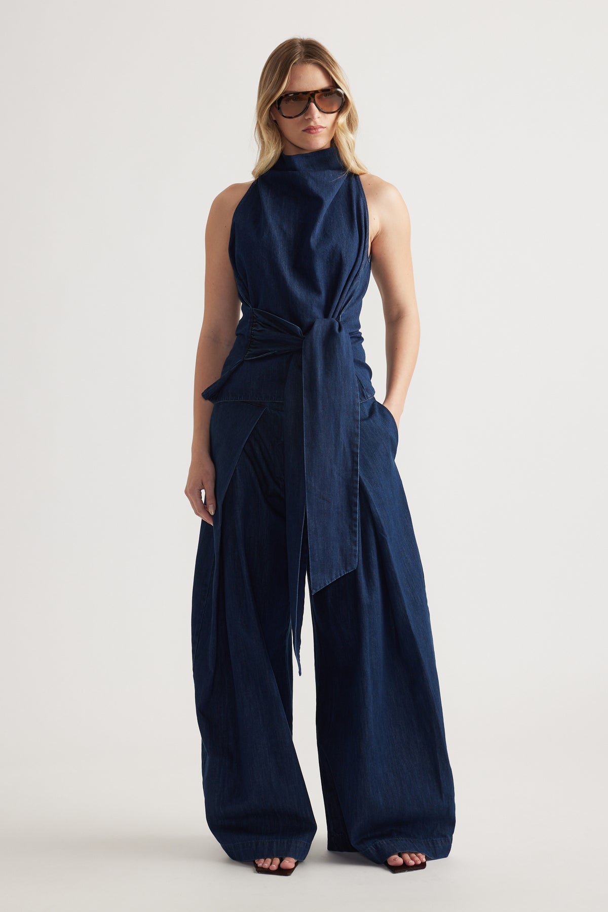 Woman wearing a navy sleeveless funnel neck top with a tie waist and wide leg trousers