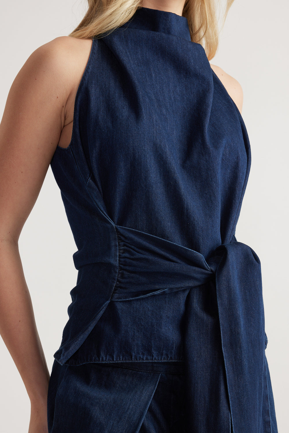Back view of a navy sleeveless funnel neck top with an adjustable waist tie