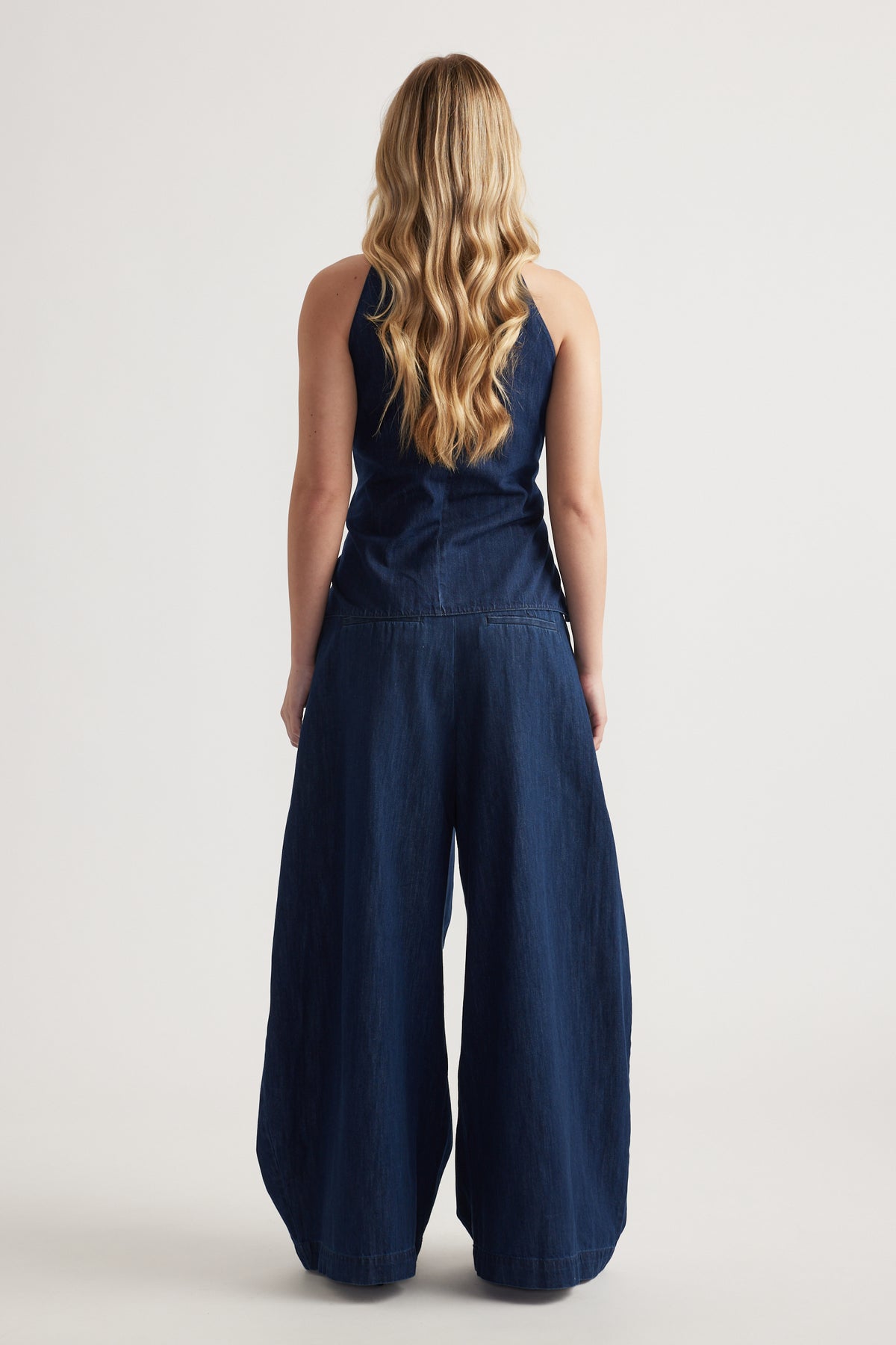 Back view of a woman wearing a navy sleeveless top with wide-leg denim pants