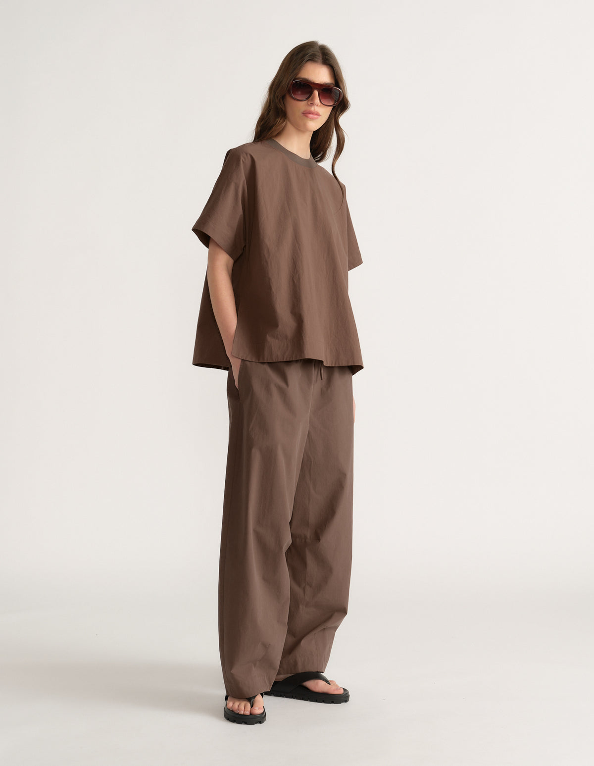 Woman wearing a chocolate brown oversized short sleeve top with matching wide leg pants and flat sandals