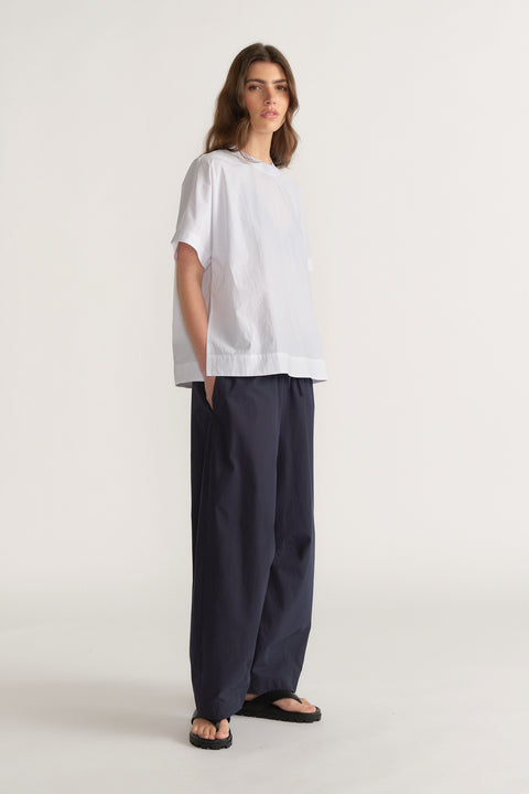 Woman wearing an oversized white short sleeve top with navy wide leg pants and black sandals