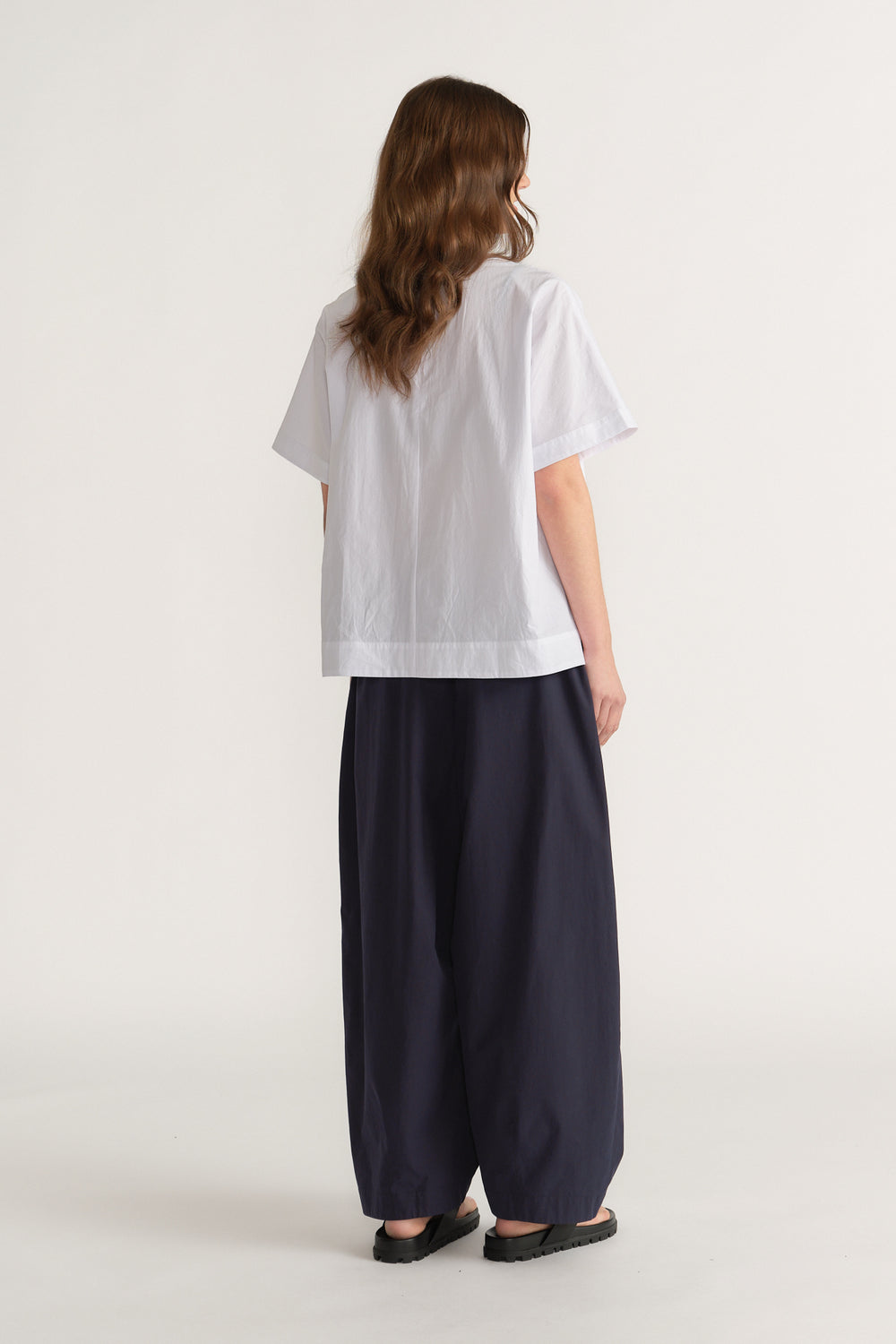 Woman wearing a relaxed white short sleeve top with wide leg navy pants and black flats