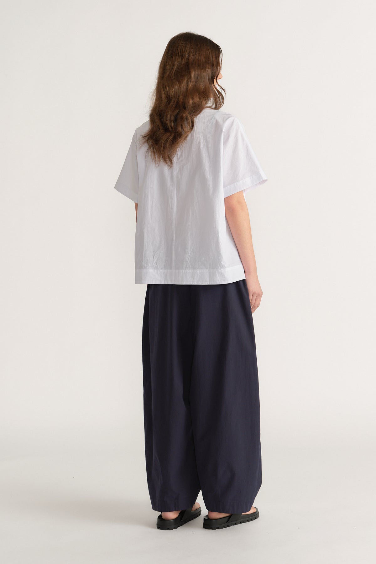 Woman wearing a relaxed white short sleeve top with wide leg navy pants and black flats