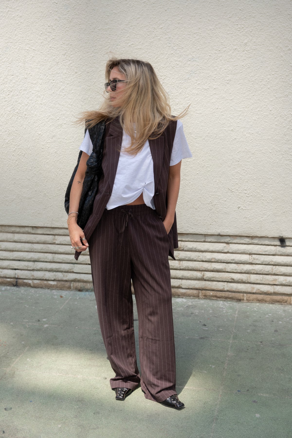 Woman wearing dark brown pinstripe wide leg pants with a white tee, brown vest and sunglasses