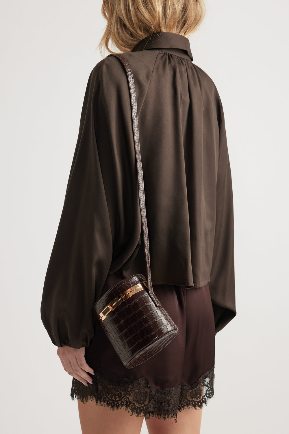 Woman wearing a dark brown loose blouse and matching lace-trimmed shorts carrying a textured dark crossbody bag