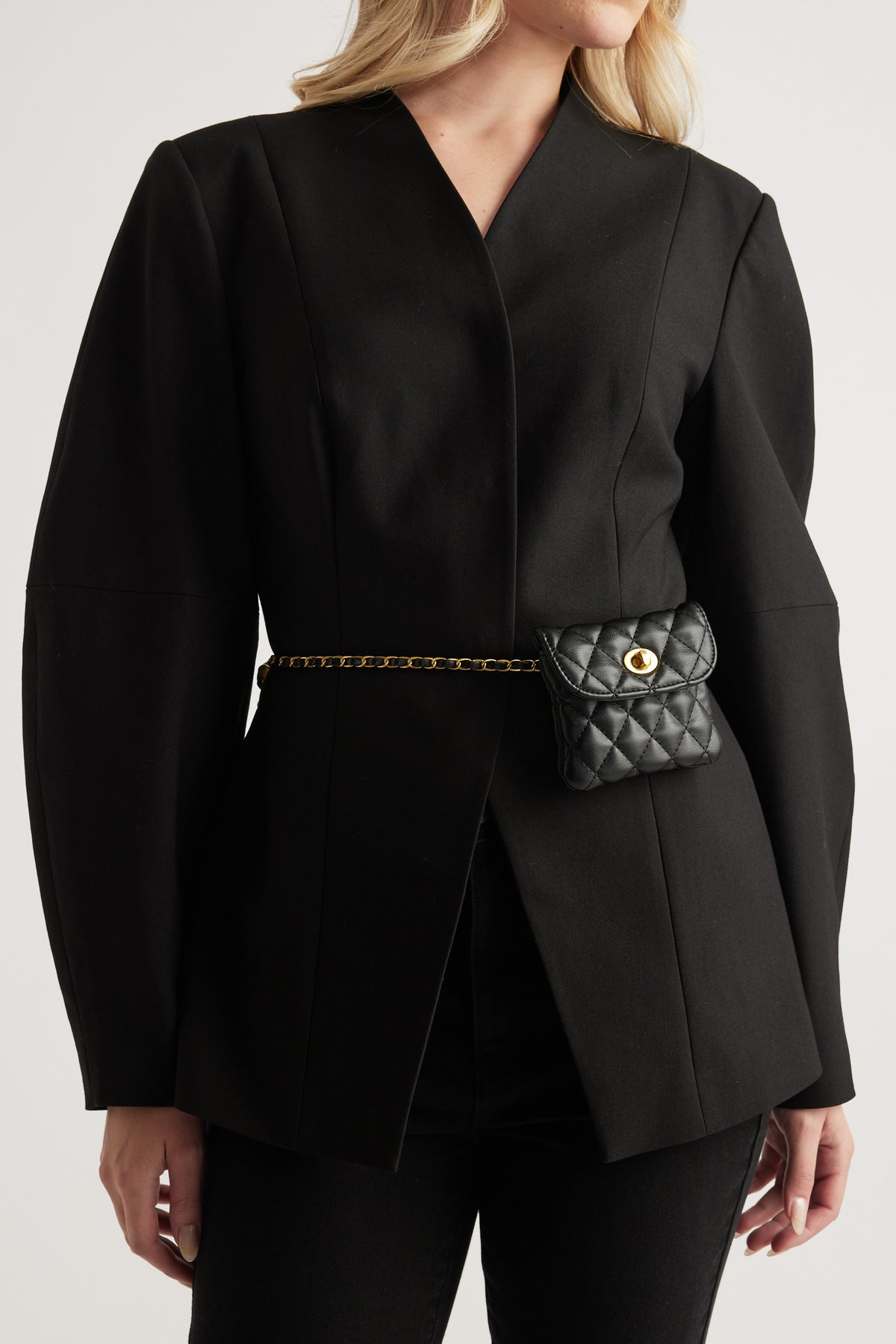 Woman wearing a black blazer and pants with a quilted mini bag belt and gold hardware