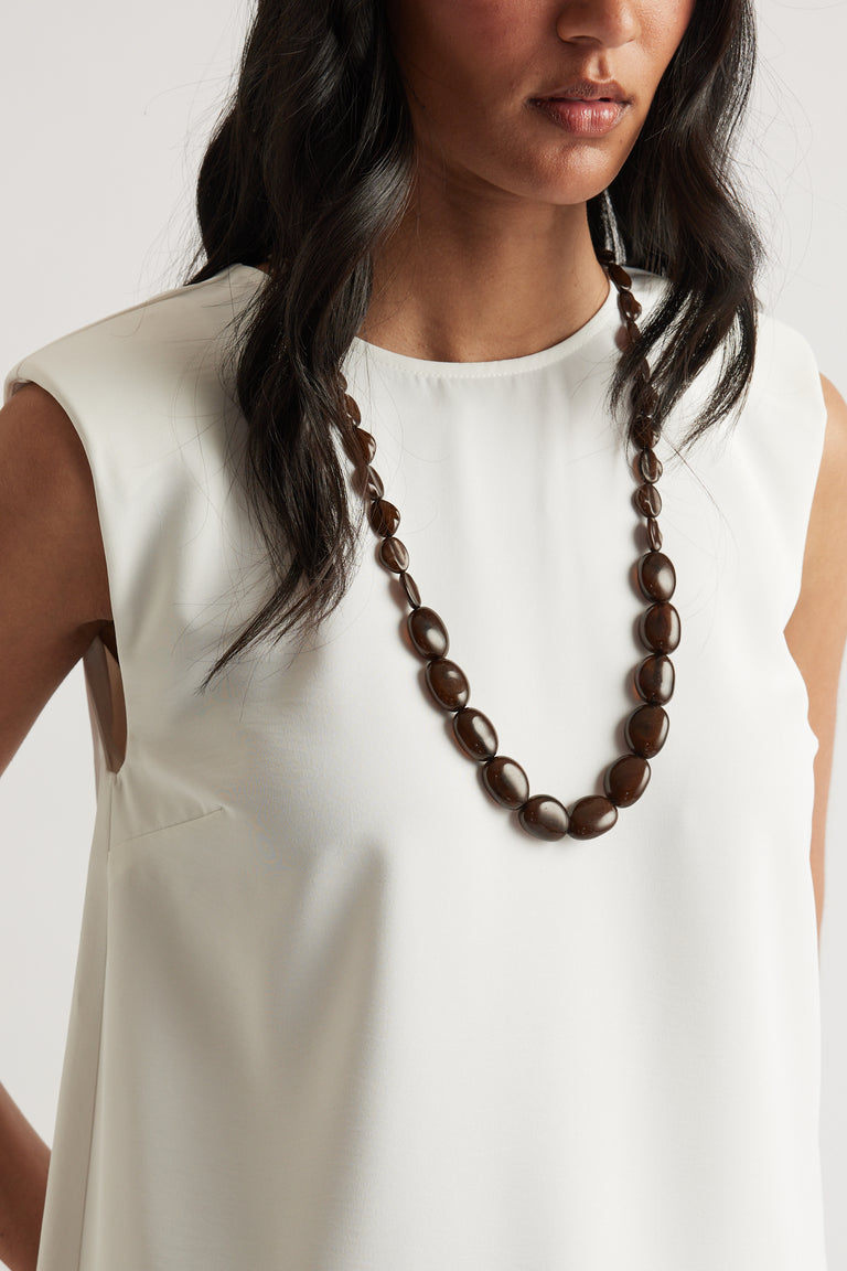 Woman wearing sleeveless white top paired with long brown resin bead necklace with extension chain