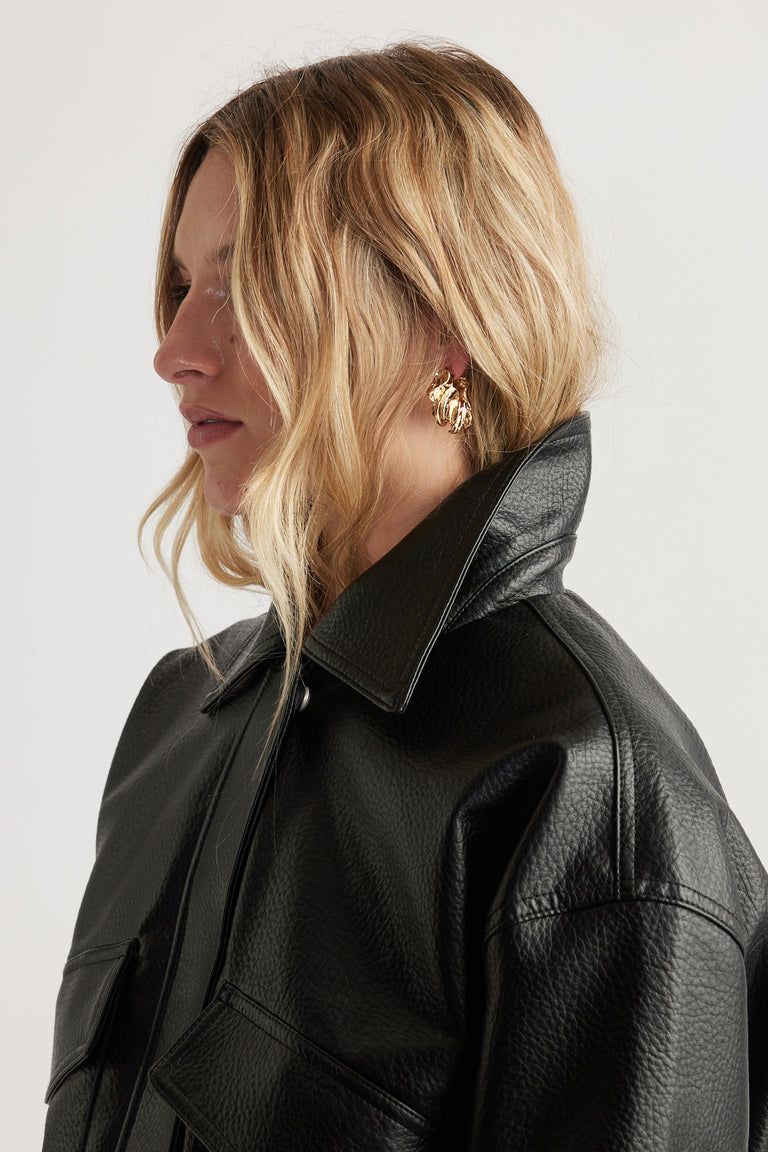 Profile of woman with wavy blonde hair wearing crinkle textured gold hoop earrings and a black textured leather jacket