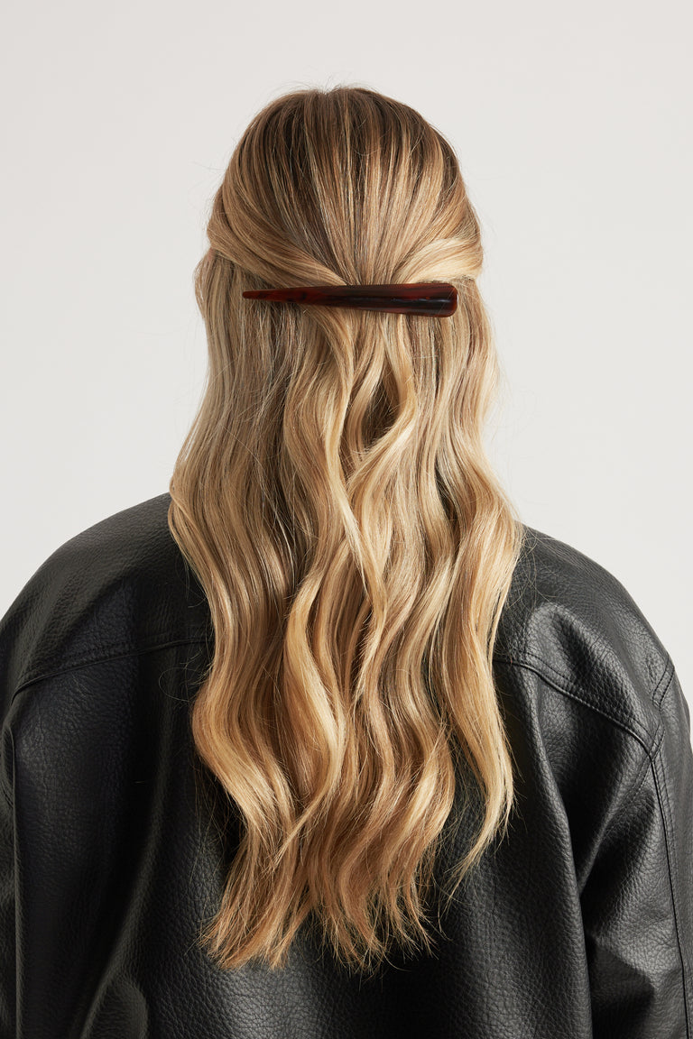Wavy blonde hair half-up secured with a sleek dark tortoiseshell claw clip worn with a black leather jacket