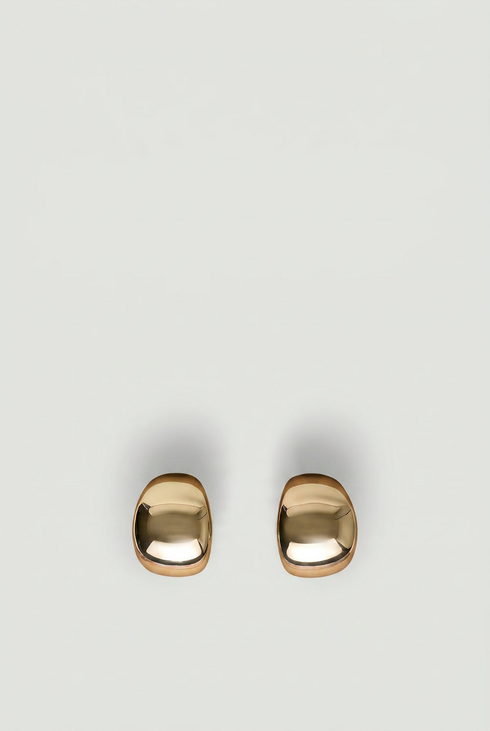 Pair of polished gold-tone statement hoop earrings with a smooth, modern rounded design on a neutral background