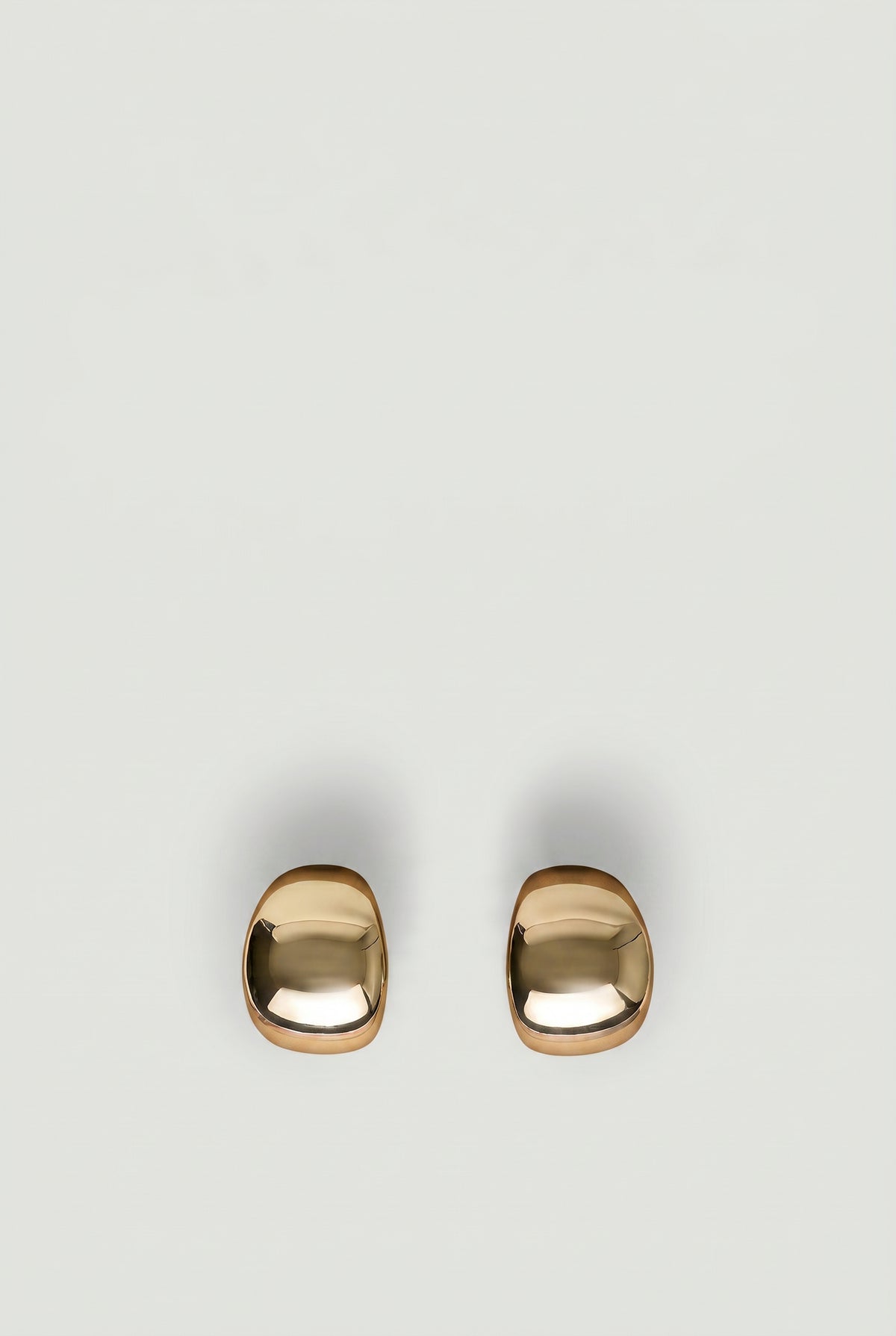 Pair of polished gold-tone statement hoop earrings with a smooth, modern rounded design on a neutral background