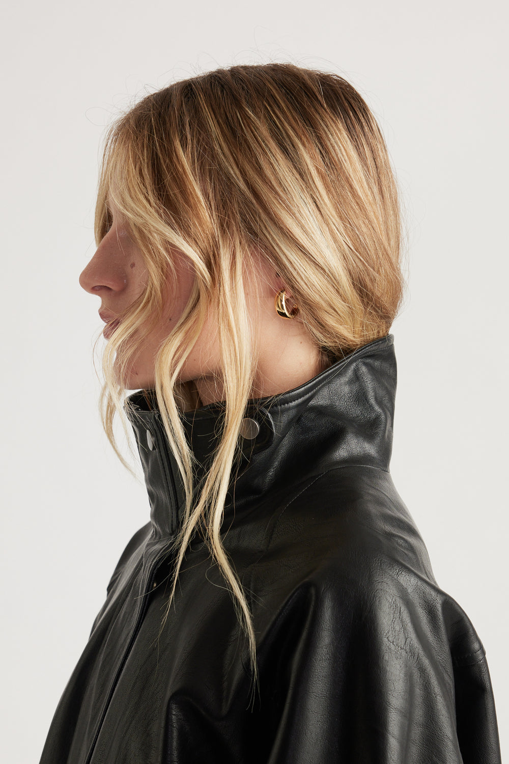 Profile of woman with blonde hair wearing gold chunky hoop earrings paired with a high-collar black leather jacket for an edgy look