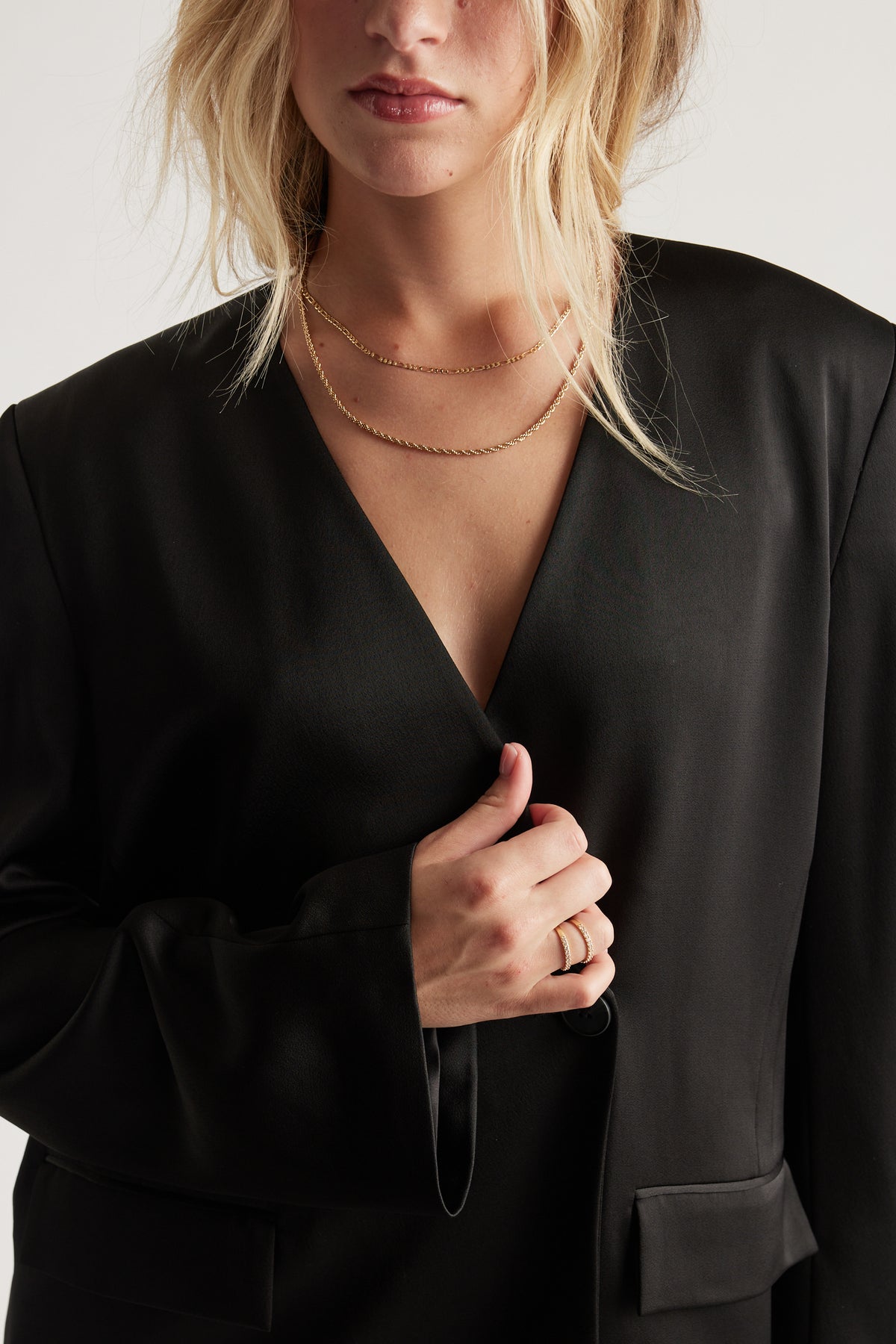 Close-up of a woman wearing layered gold necklaces and two elegant gold rings with diamante details.