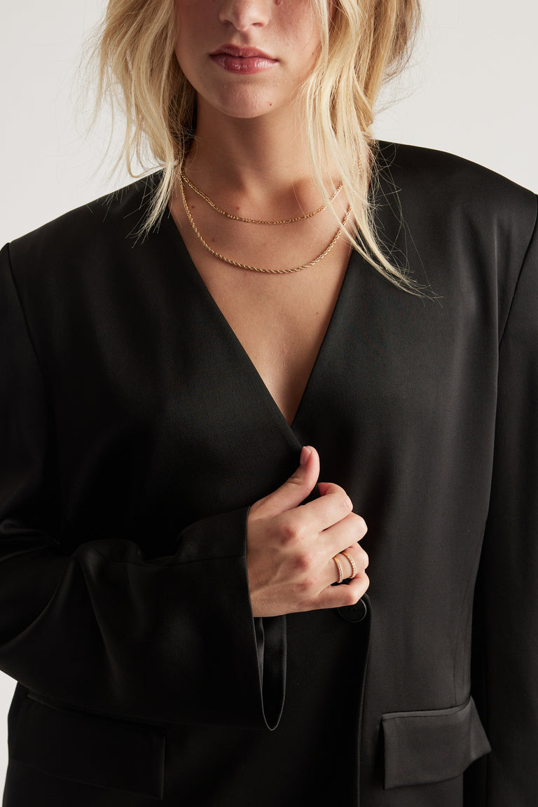 Close-up of a woman wearing layered gold necklaces and two elegant gold rings with diamante details.
