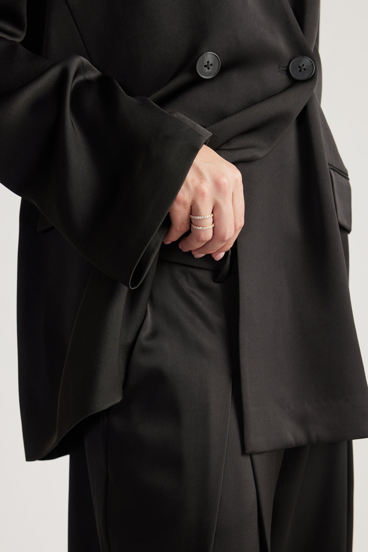 Hand adorned with two delicate 9ct gold rings featuring sparkling diamante details, styled with a black blazer and pants.