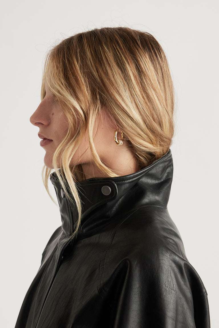 Side profile of a woman wearing gold-toned stone hoop earrings with tousled blonde hair and a black high-collar jacket