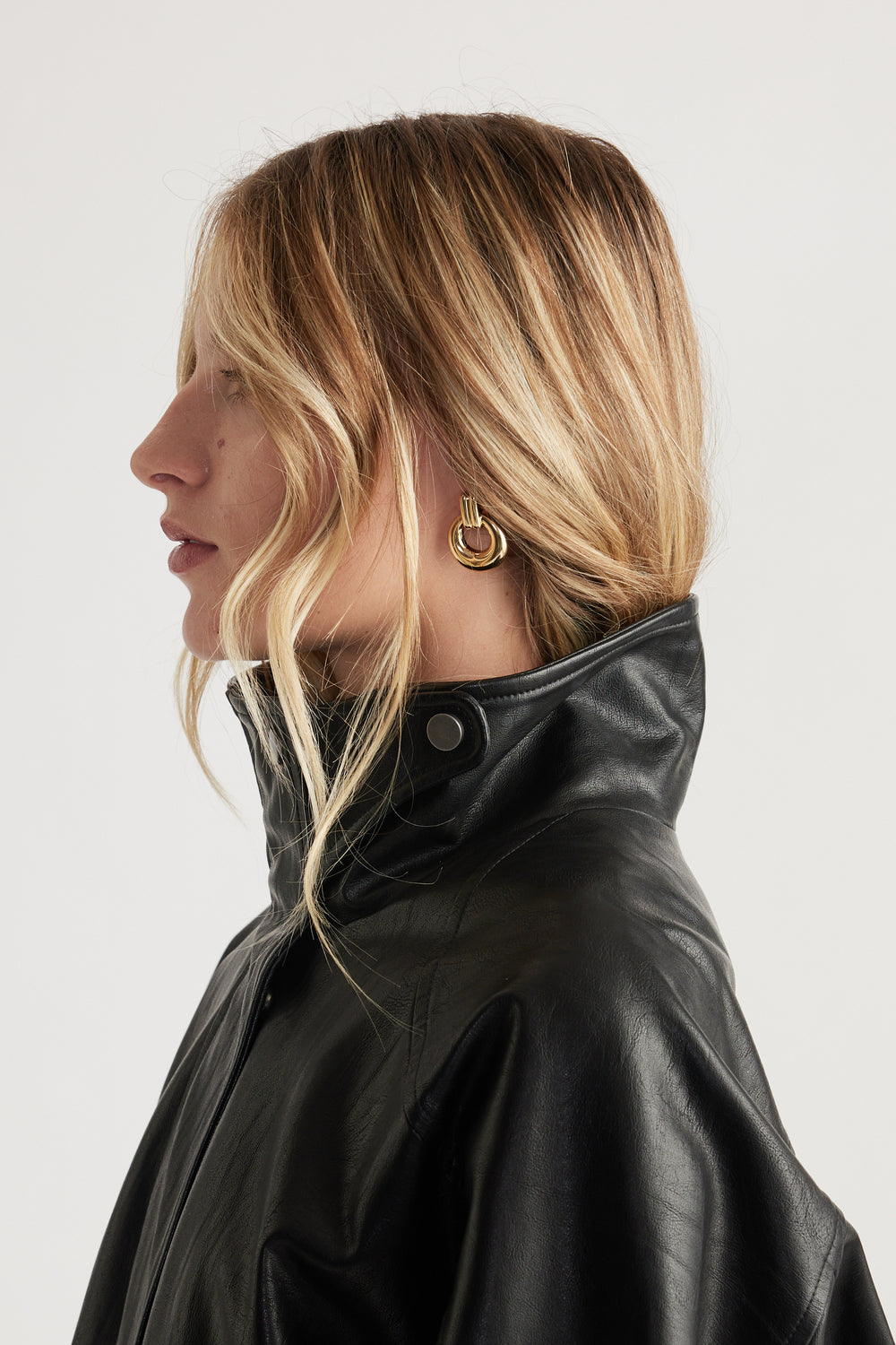 Profile view of woman wearing gold hoop door knocker earrings paired with a high-collar black leather jacket
