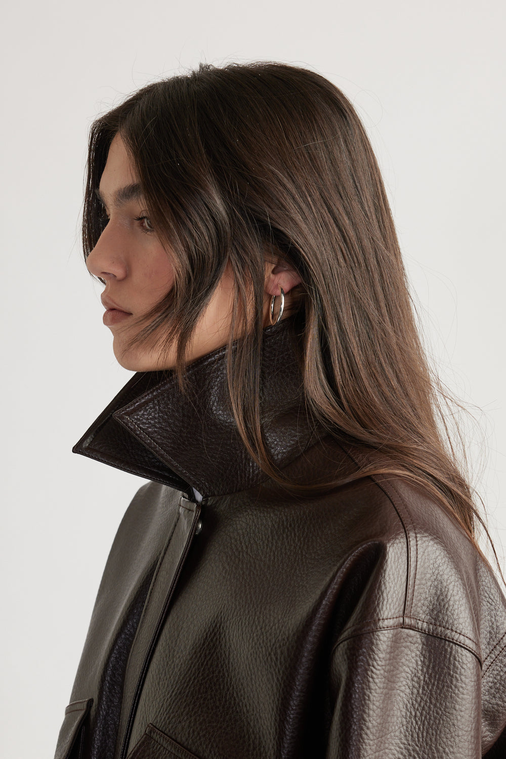 Profile view of a woman wearing sleek silver hoop earrings paired with a dark textured leather jacket collar raised