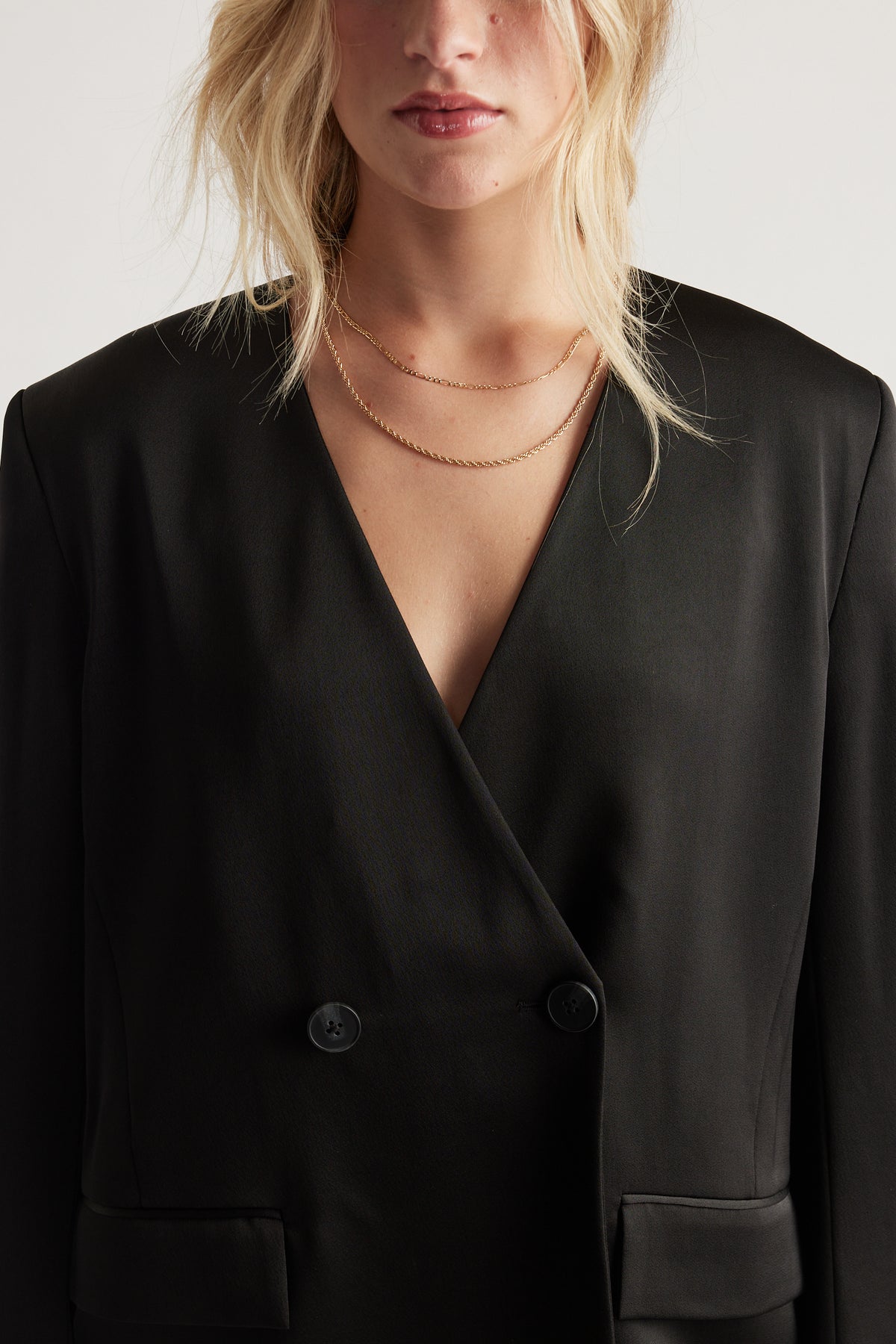 Close-up of a woman wearing layered delicate gold chains over a sleek black blazer with a deep V neckline
